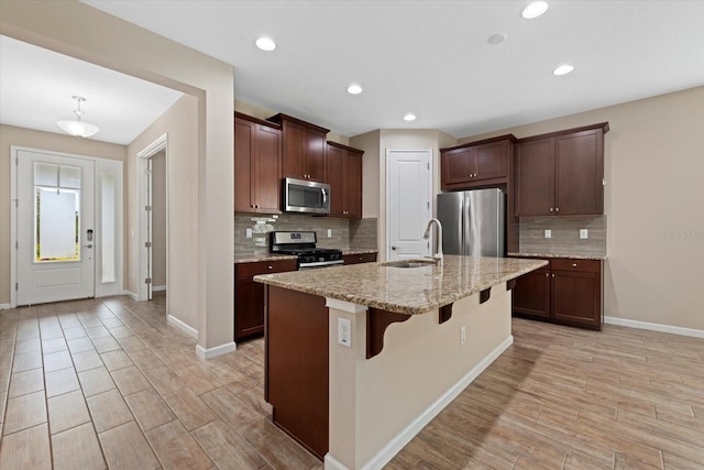 kitchen with sink, light stone counters, a center island with sink, appliances with stainless steel finishes, and a kitchen breakfast bar