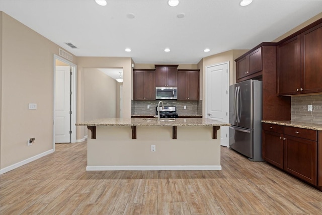 kitchen featuring a kitchen island with sink, light stone counters, stainless steel appliances, and a kitchen breakfast bar