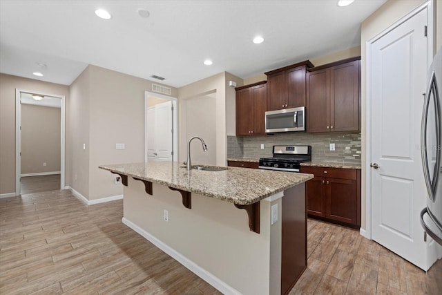 kitchen with sink, appliances with stainless steel finishes, a kitchen island with sink, a kitchen breakfast bar, and light stone counters