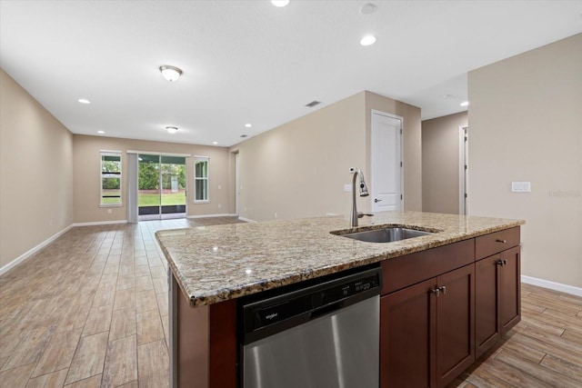 kitchen featuring light stone counters, a kitchen island with sink, dishwasher, and sink