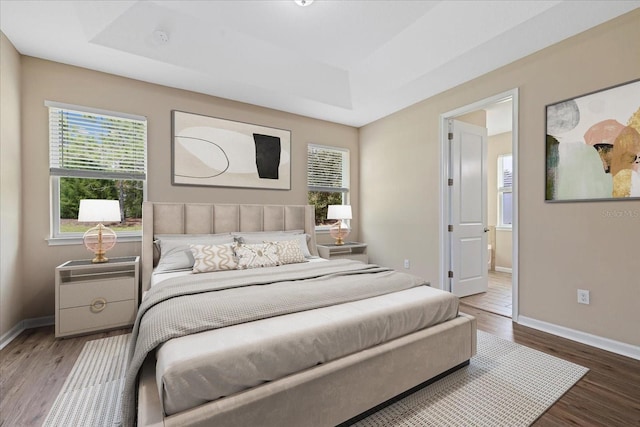 bedroom featuring hardwood / wood-style flooring, ensuite bathroom, and a tray ceiling