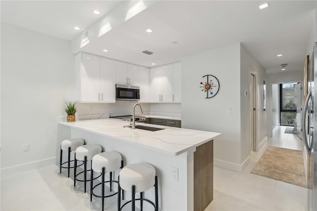 kitchen featuring sink, a breakfast bar area, white cabinetry, stainless steel appliances, and kitchen peninsula