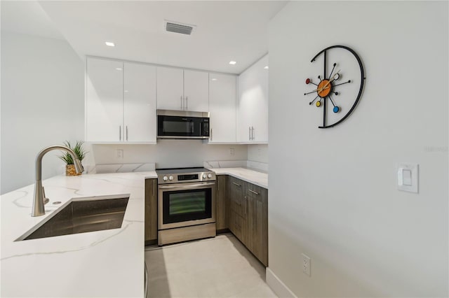 kitchen with light stone counters, stainless steel appliances, sink, and white cabinets