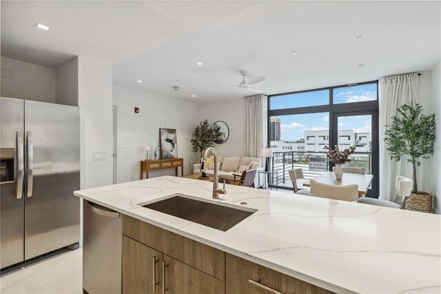 kitchen featuring sink, ceiling fan, stainless steel appliances, floor to ceiling windows, and light stone countertops