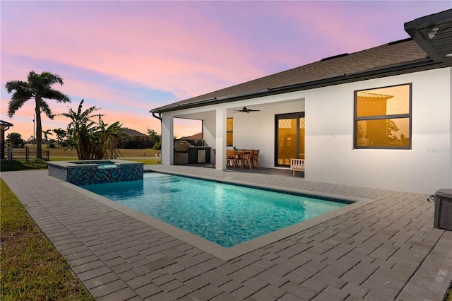 pool at dusk with an in ground hot tub, area for grilling, ceiling fan, and a patio area