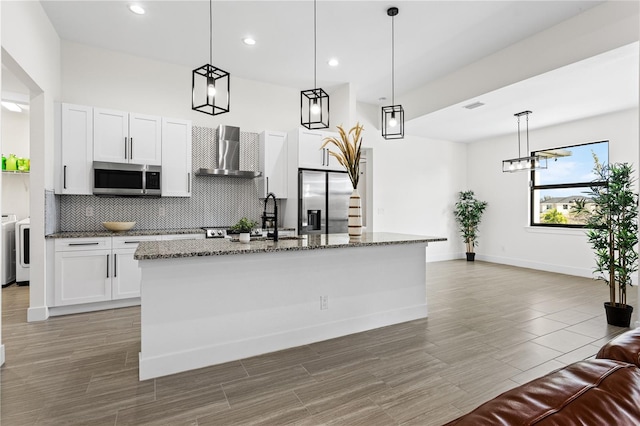 kitchen with a kitchen island with sink, pendant lighting, stainless steel appliances, and wall chimney exhaust hood