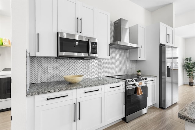 kitchen with wall chimney exhaust hood, stainless steel appliances, stone counters, and white cabinets