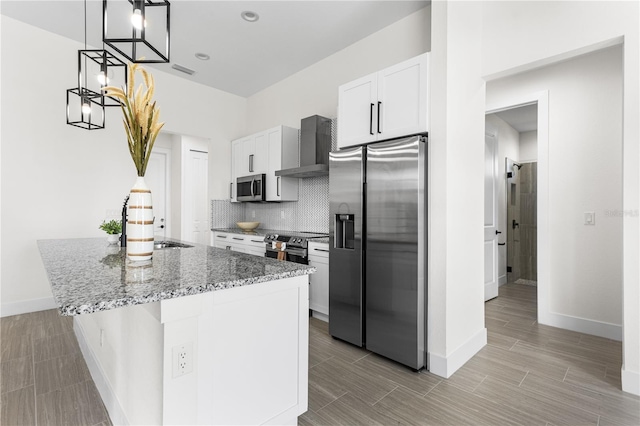 kitchen with decorative light fixtures, appliances with stainless steel finishes, a kitchen island, white cabinets, and wall chimney range hood