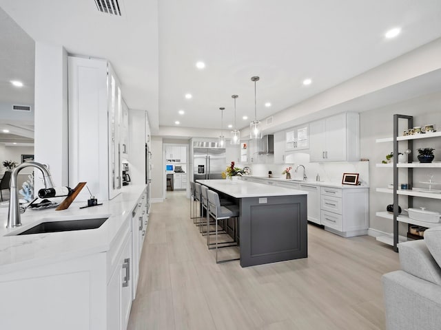 kitchen featuring a spacious island, wall chimney exhaust hood, sink, white cabinetry, and hanging light fixtures