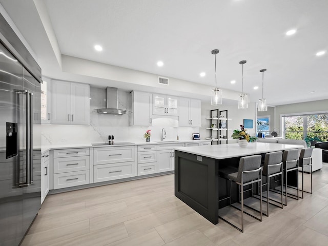 kitchen featuring white cabinetry, sink, hanging light fixtures, wall chimney exhaust hood, and a spacious island