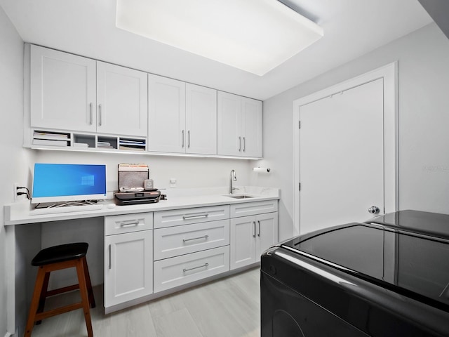 kitchen featuring black range with electric stovetop, sink, white cabinets, and light hardwood / wood-style flooring