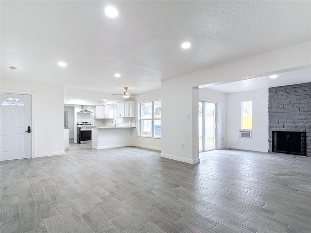 unfurnished living room with a brick fireplace, a textured ceiling, and ceiling fan