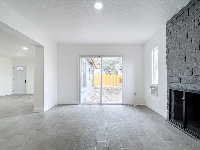 unfurnished living room with a brick fireplace, a wall mounted AC, and a textured ceiling