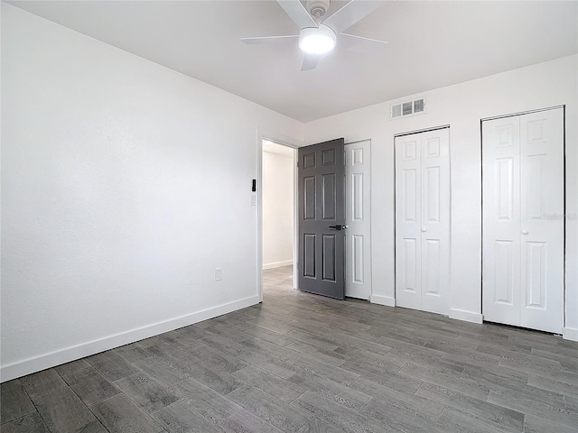 unfurnished bedroom with ceiling fan, wood-type flooring, and two closets