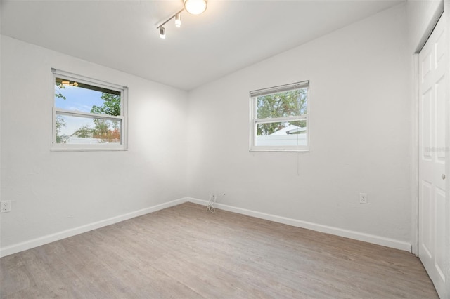 empty room with lofted ceiling, rail lighting, light wood-type flooring, and a wealth of natural light