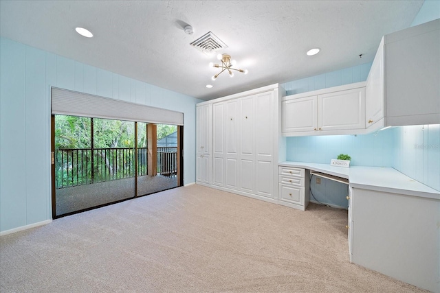 unfurnished office featuring light carpet, built in desk, and a textured ceiling