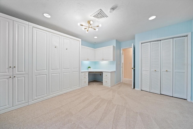 unfurnished bedroom with built in desk, a chandelier, multiple closets, light carpet, and a textured ceiling