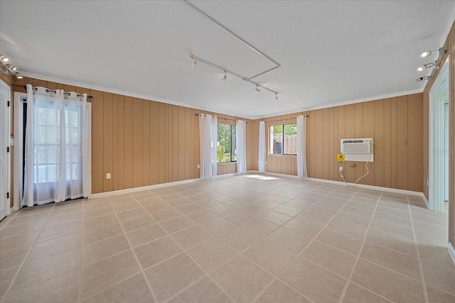 empty room with rail lighting, a wall mounted air conditioner, wood walls, and light tile patterned floors