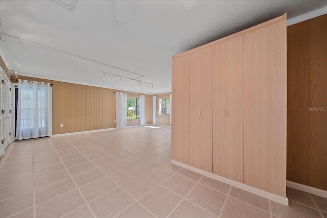 tiled empty room featuring rail lighting and wood walls