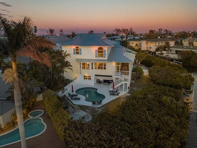 back house at dusk featuring a swimming pool with hot tub, a patio, and a balcony