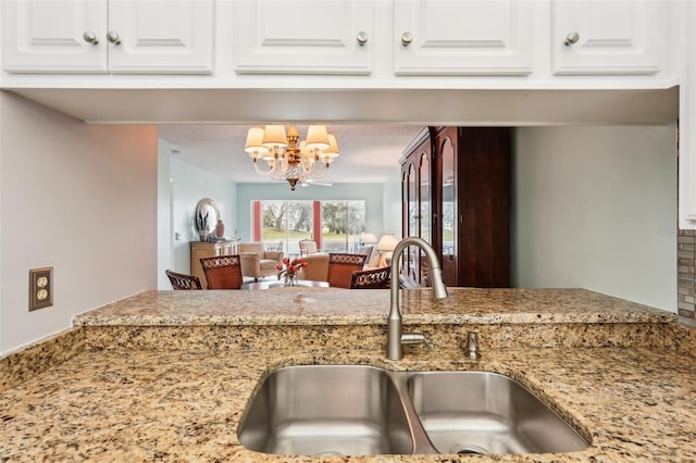 kitchen with an inviting chandelier, white cabinetry, sink, and light stone counters