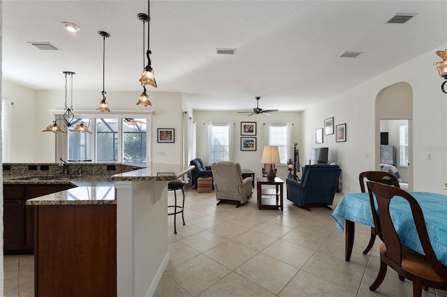 kitchen featuring a breakfast bar, ceiling fan, light tile patterned flooring, decorative light fixtures, and dark stone counters