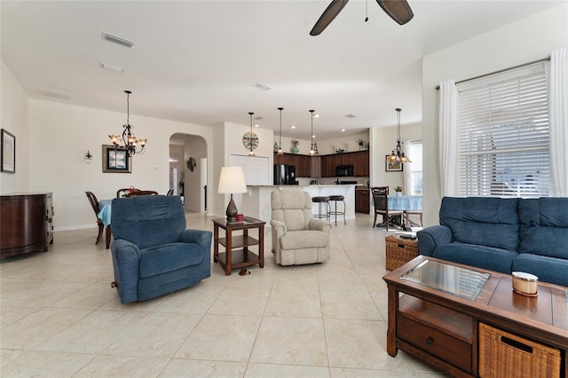 tiled living room with ceiling fan with notable chandelier