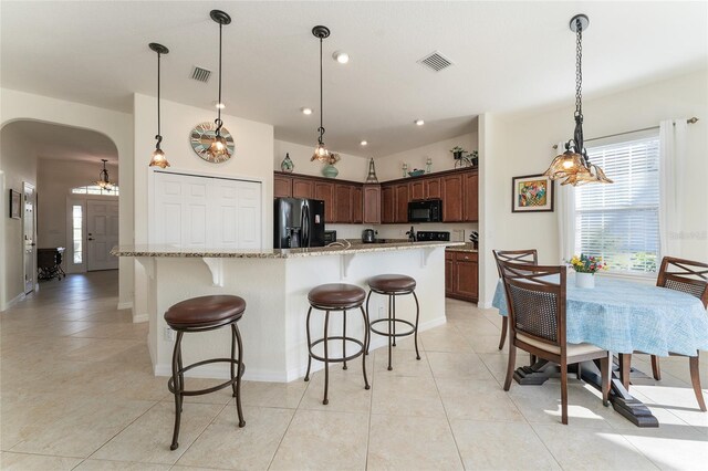 kitchen with a center island with sink, pendant lighting, light stone counters, and black appliances