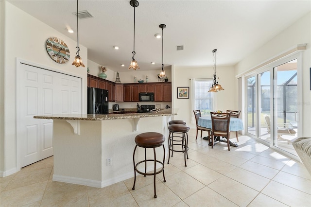 kitchen featuring pendant lighting, light tile patterned flooring, light stone counters, and black appliances