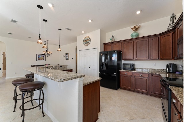 kitchen with pendant lighting, light stone counters, black appliances, and an island with sink