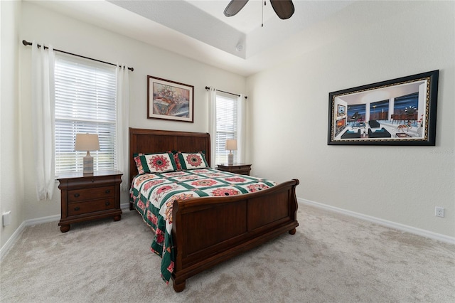 bedroom with light carpet, a tray ceiling, and ceiling fan