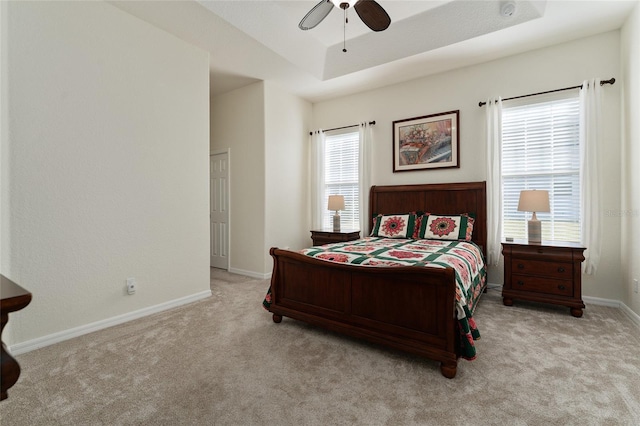 bedroom with ceiling fan, light colored carpet, and a raised ceiling