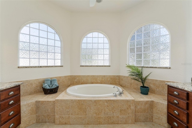 bathroom with vanity, tiled tub, and ceiling fan