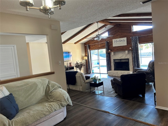 living room featuring dark wood-type flooring, a stone fireplace, lofted ceiling with beams, a textured ceiling, and ceiling fan with notable chandelier