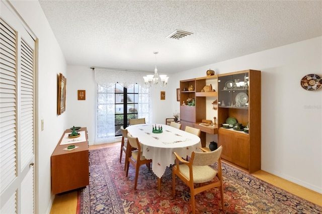 dining area featuring wood-type flooring, a chandelier, and a textured ceiling