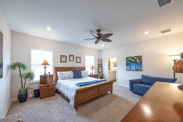 bedroom with multiple windows, ceiling fan, light colored carpet, and ensuite bath