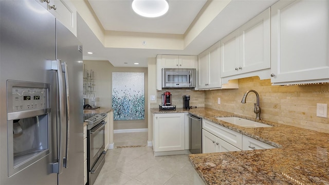 kitchen with sink, appliances with stainless steel finishes, white cabinetry, light stone countertops, and a raised ceiling