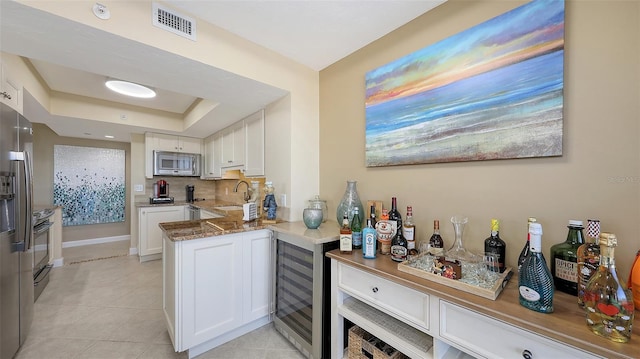 kitchen with stainless steel appliances, white cabinets, beverage cooler, and kitchen peninsula