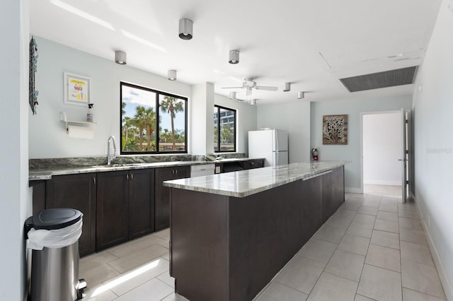 kitchen with light tile patterned flooring, sink, a center island, light stone counters, and white appliances