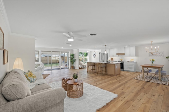 living area featuring ceiling fan with notable chandelier, visible vents, baseboards, light wood-style floors, and crown molding