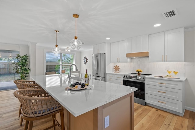 kitchen featuring pendant lighting, appliances with stainless steel finishes, a kitchen island with sink, white cabinetry, and light stone countertops