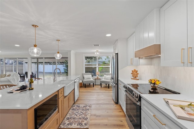 kitchen featuring pendant lighting, a center island with sink, appliances with stainless steel finishes, white cabinets, and exhaust hood