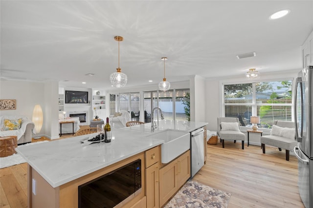 kitchen featuring light stone counters, open floor plan, hanging light fixtures, appliances with stainless steel finishes, and an island with sink