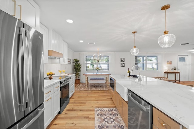 kitchen with a sink, white cabinets, appliances with stainless steel finishes, light stone countertops, and pendant lighting