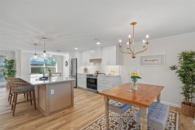 kitchen featuring stainless steel appliances, light countertops, hanging light fixtures, white cabinets, and a kitchen island with sink