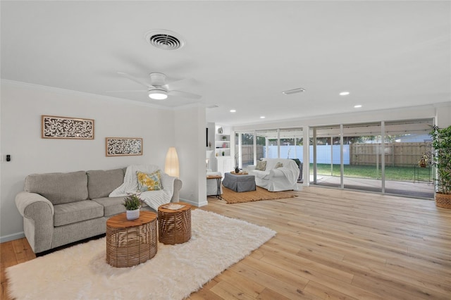 living room with crown molding, baseboards, visible vents, and light wood-style floors