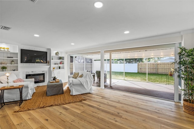 living area featuring recessed lighting, a fireplace, visible vents, light wood finished floors, and crown molding