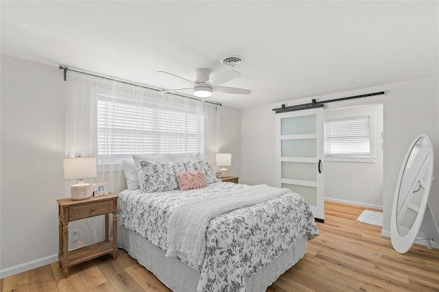 bedroom with a barn door, visible vents, baseboards, ceiling fan, and light wood-style flooring