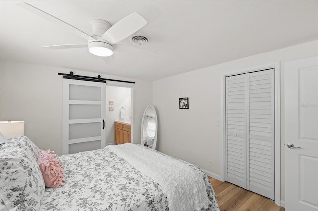 bedroom with light wood finished floors, a barn door, visible vents, a ceiling fan, and a closet