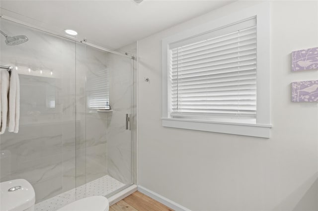 bathroom with wood finished floors, a marble finish shower, toilet, and baseboards